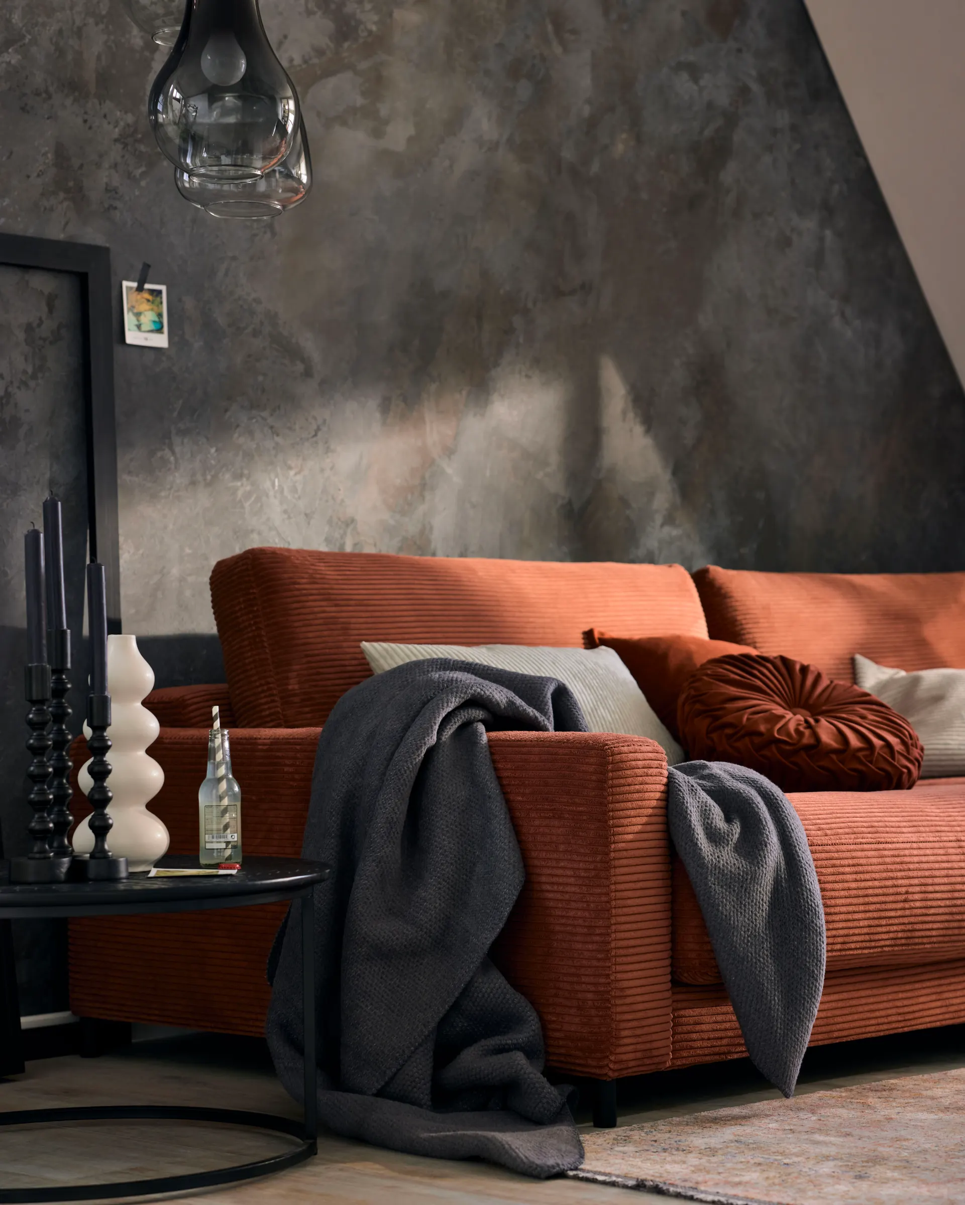 Rostrotes Sofa mit Kissen und Decke vor einer dunklen Wand