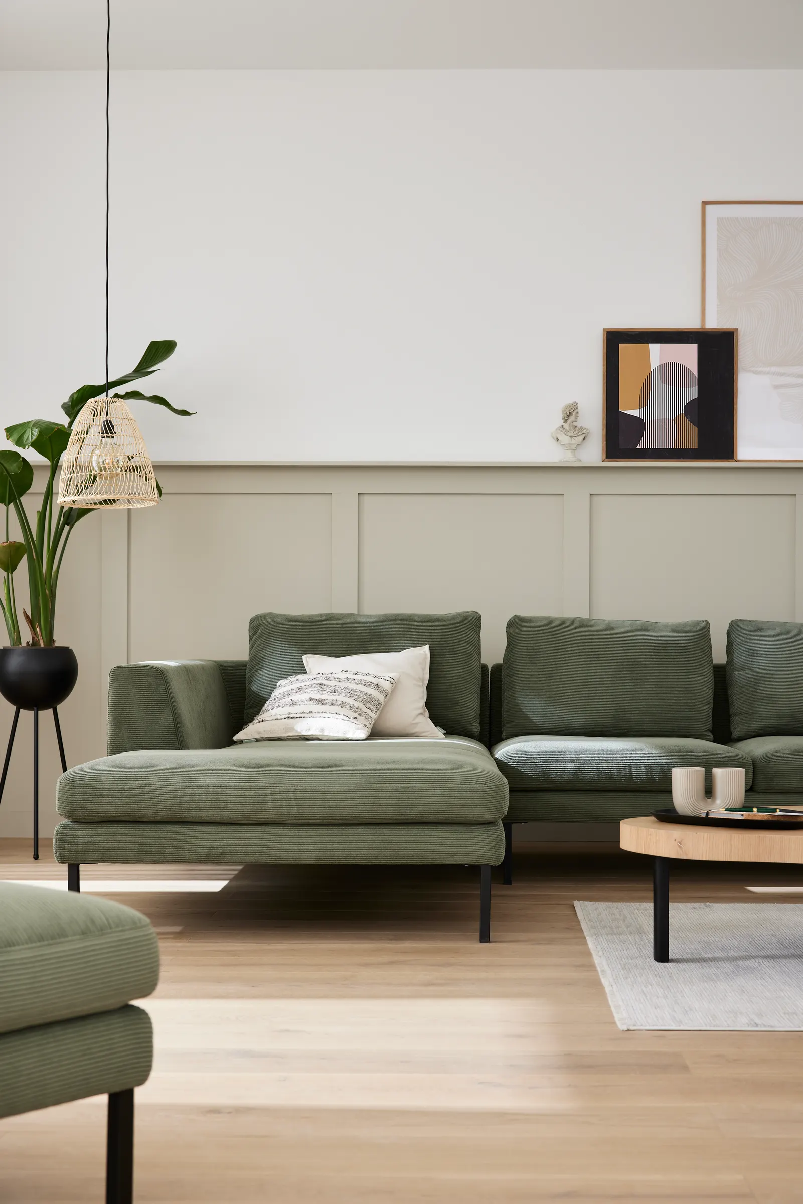 Grünes Ecksofa mit Ottomane vor heller Wandvertäfelung
