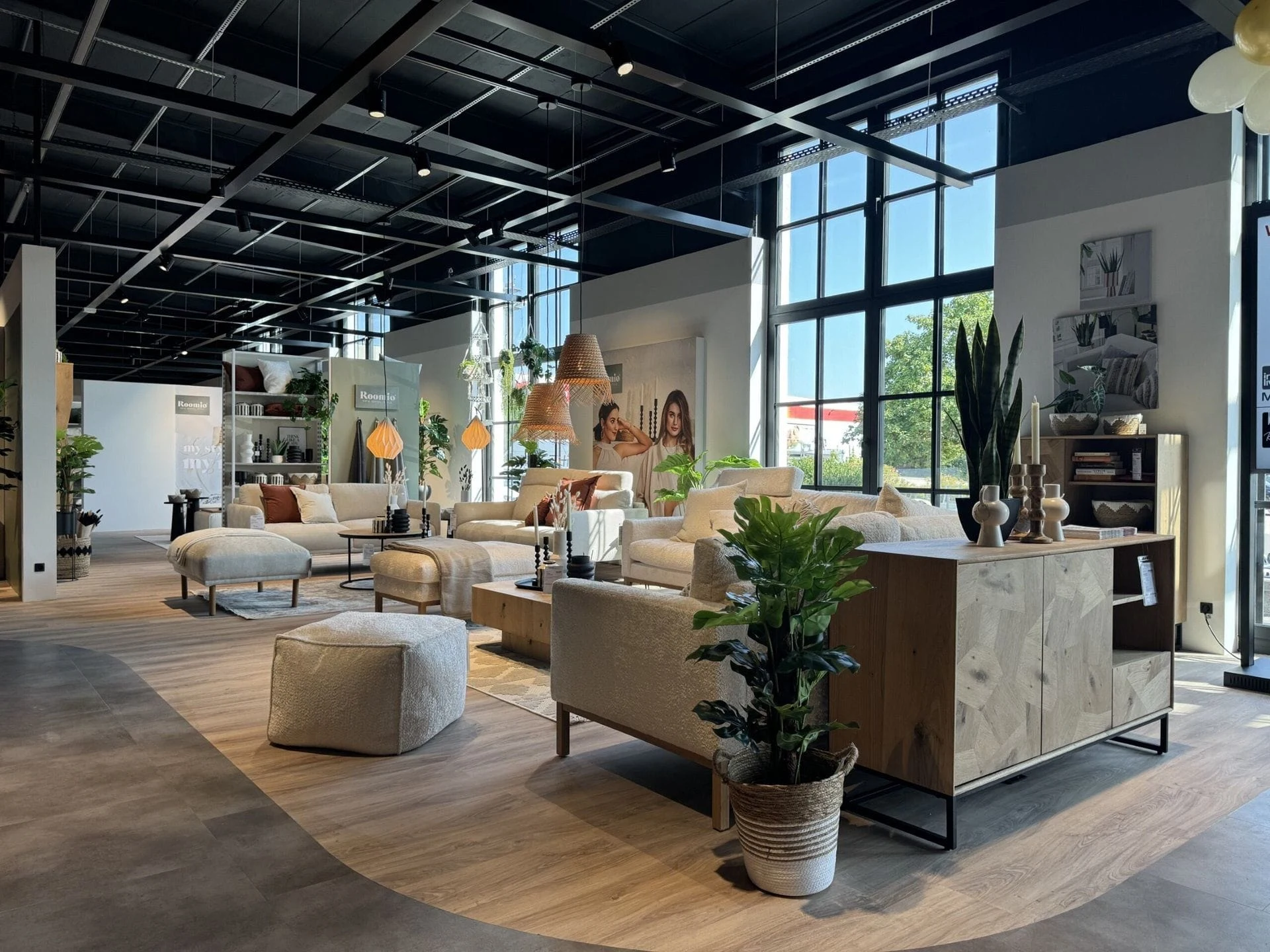 Heller Roomio Ausstellungsraum mit Sofas, Sesseln und Wohnaccessoires unter hohen Fenstern.