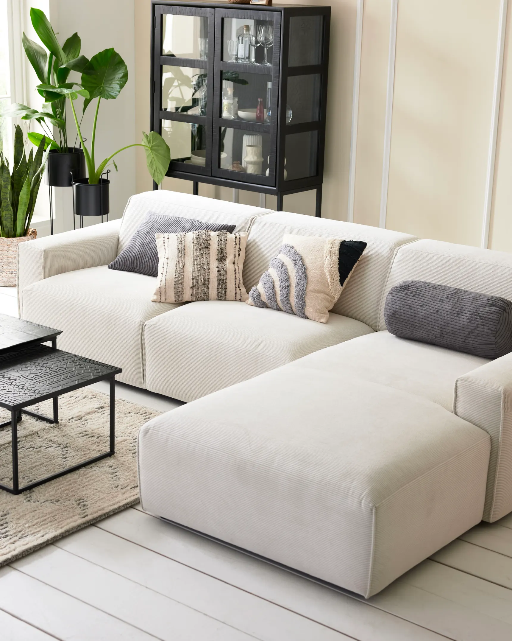 Weißes Ecksofa mit Ottomane, schwarzen Beistelltischen und Vitrine