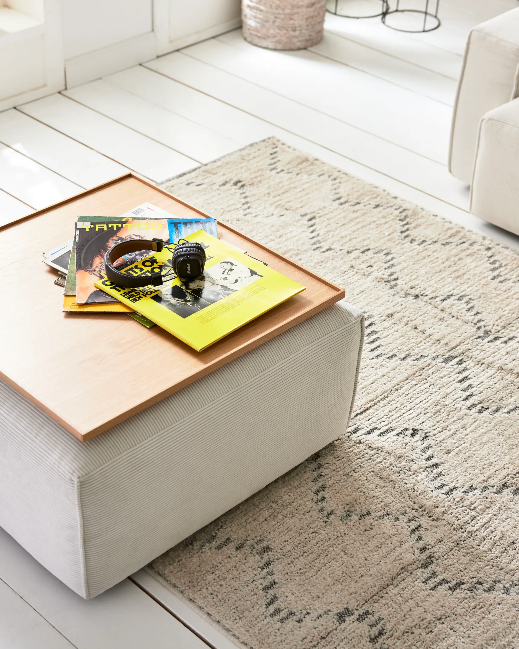 Heller gemusterter Teppich mit Hocker und einem Tablett mit Zeitschriften